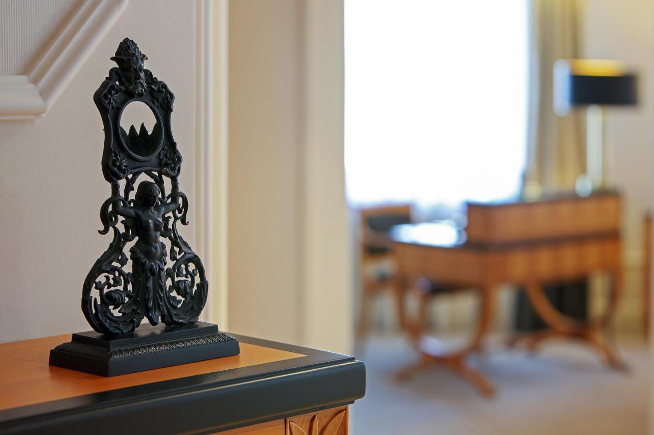 Отель The Westin Grand Берлин Экстерьер фото The photo shows a decorative black object, possibly a sculpture or a stand, placed on a surface. The object features intricate designs, including a central figure and ornate detailing. In the background, there is a blurred view of a room with light-c