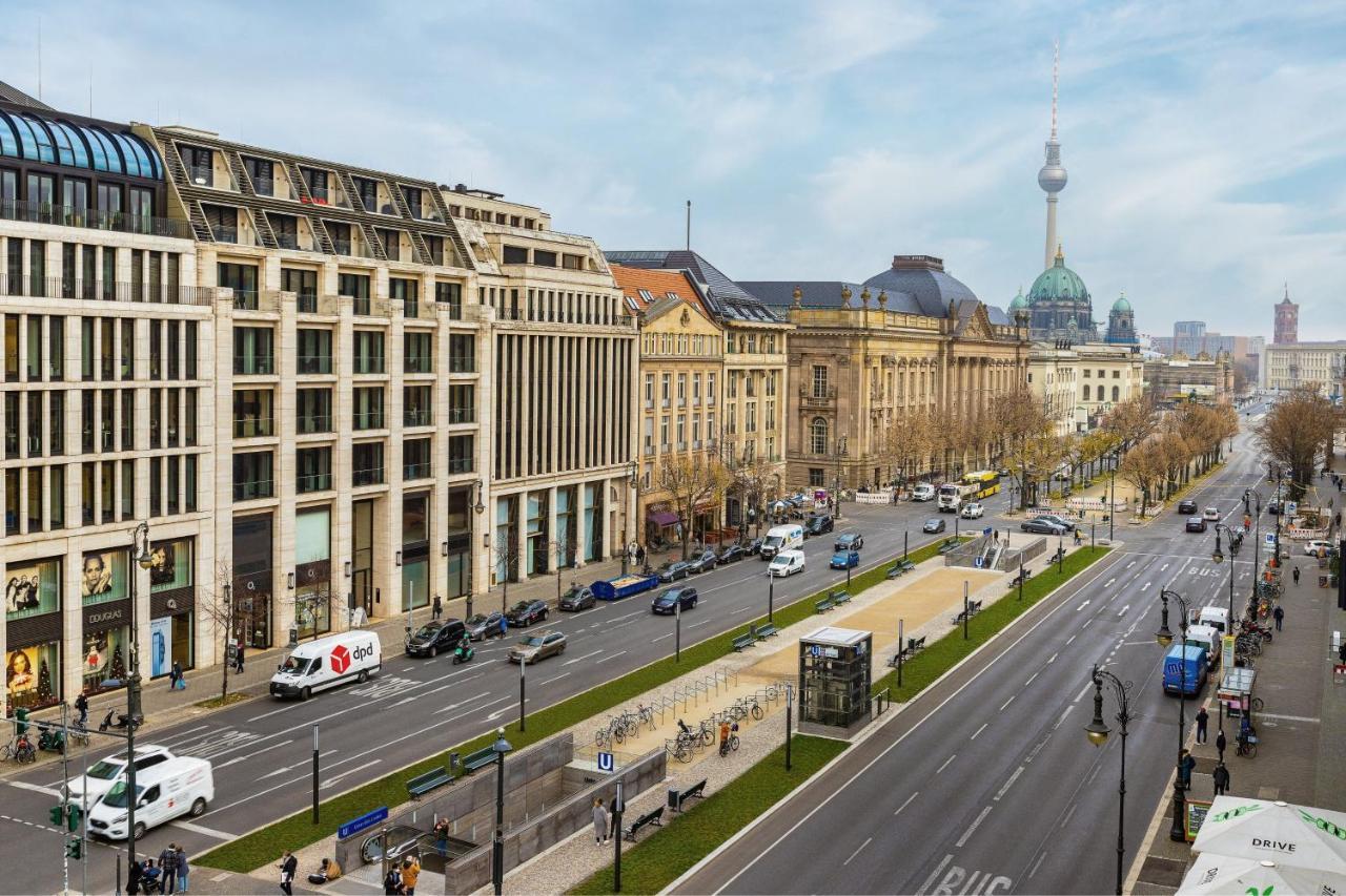 Отель The Westin Grand Берлин Экстерьер фото The photo shows a wide urban street with a mix of modern and historic buildings on either side. The foreground features a wide road with traffic, including cars and vans. On the left, there are contemporary architectural designs, while on the right, 