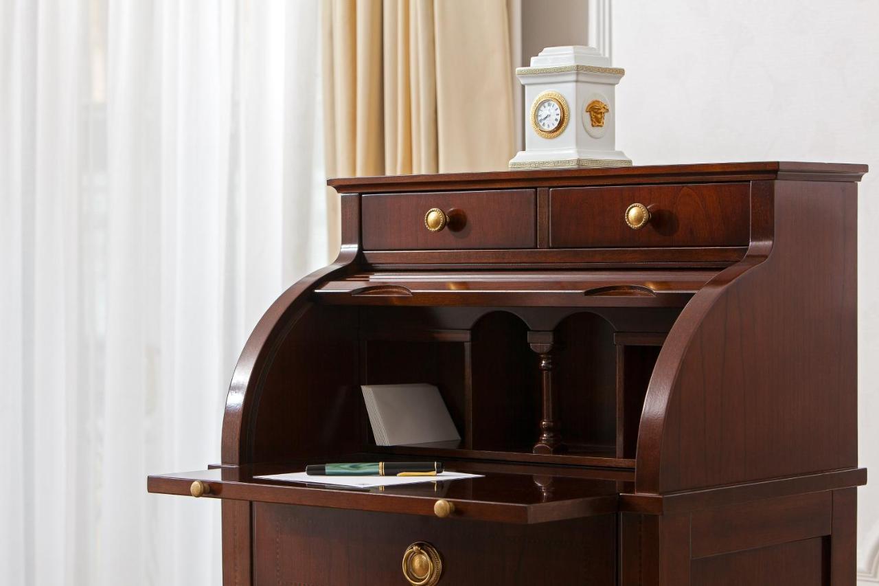 Отель The Westin Grand Берлин Экстерьер фото The image shows a wooden writing desk with a rich, dark finish. The desk features a curved front and an open compartment above a flat writing surface. There are two small drawers at the top, each with round brass handles. On the desk, there is a shee